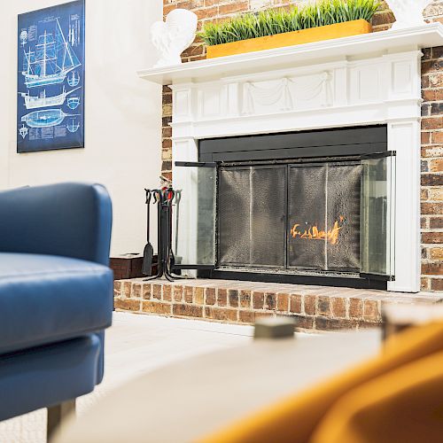 A living room with a blue armchair, a fireplace featuring a fireguard, a framed picture, and various decor items.