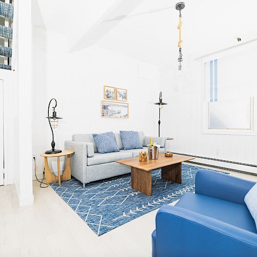 A bright, modern living room with blue and white decor, featuring a sofa, armchair, coffee table, and wall art, plus distinctive lighting fixtures.