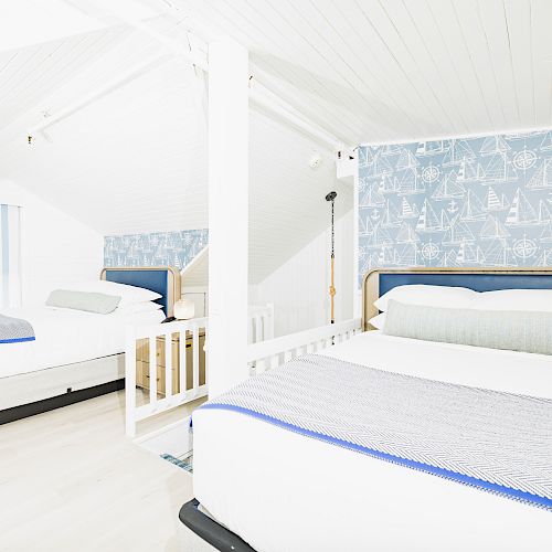 A bright, white bedroom with two double beds, blue and white bedding, and maritime-themed wallpaper featuring sailboats.