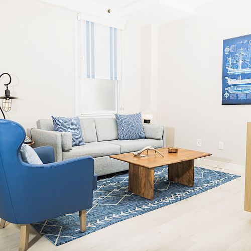 A modern living room with blue and gray furniture, a wooden coffee table, and a nautical-themed wall art.