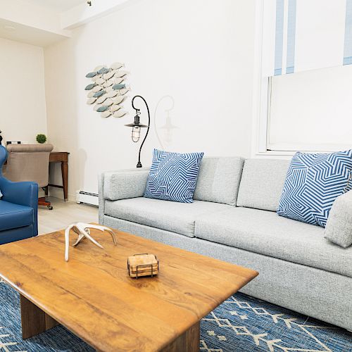 A living room with a gray sofa, blue armchair, wooden coffee table, and coastal decorations on the wall and cushions, featuring a minimalist style.