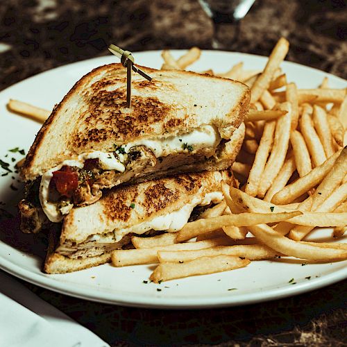 A sandwich filled with melted cheese and vegetables, cut in half and secured with a toothpick, served with a side of French fries on a plate.