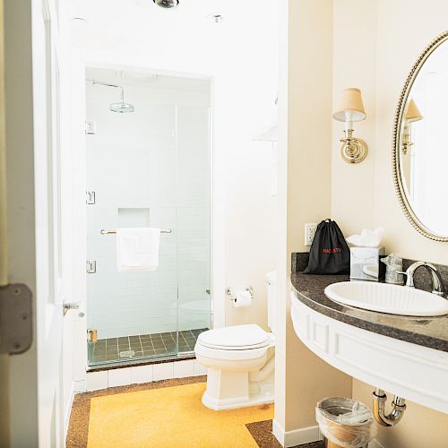 This image shows a clean, well-lit bathroom with a glass-enclosed shower, a toilet, a vanity with a sink, and a round mirror above the sink.