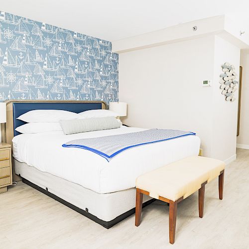 A modern bedroom with a large bed, blue-themed wallpaper, bedside tables with lamps, and an orange bench at the foot of the bed.