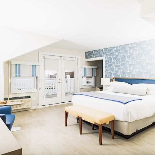 A bright, modern hotel room with a king-sized bed, blue and white decor, a work desk, and large windows leading to a balcony in the image.