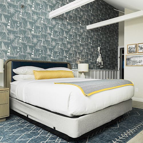 A well-decorated bedroom with a patterned wallpaper, a bed, nightstands, lamps, and wall art; color scheme includes blue, white, and yellow accents.