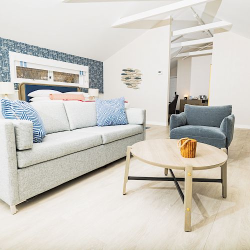 A modern living room with a grey sofa, blue armchair, round coffee table, and blue-patterned accent wall.