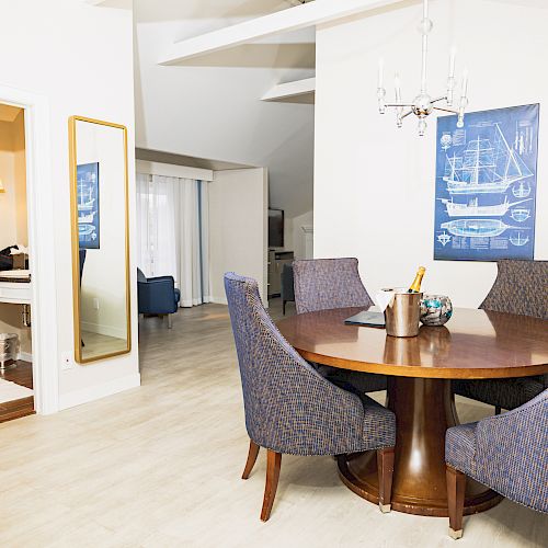 The image shows a dining area with a round table and four chairs, adjacent to a bathroom. The room has nautical decor and a modern design.