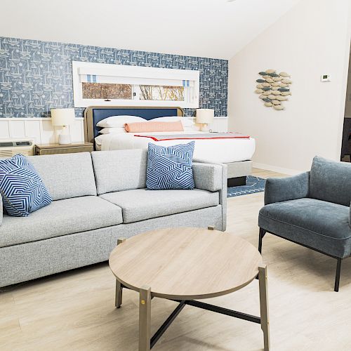 A modern bedroom with a gray sofa, blue armchair, wooden coffee table, and a bed in the background against a patterned blue wall ends the sentence.