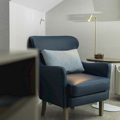 The image shows a blue armchair with a pillow, a side table with a lamp, and an air conditioner against a light-colored wall.