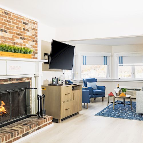 A cozy living room with a brick fireplace, wall-mounted TV, blue chairs, a gray sofa, and large windows with striped shades, ends the sentence.