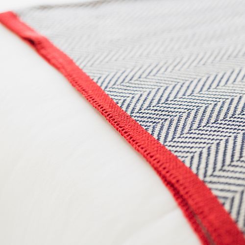 A close-up of a herringbone-patterned fabric, featuring a blue and white design with a red border, placed on a white surface.