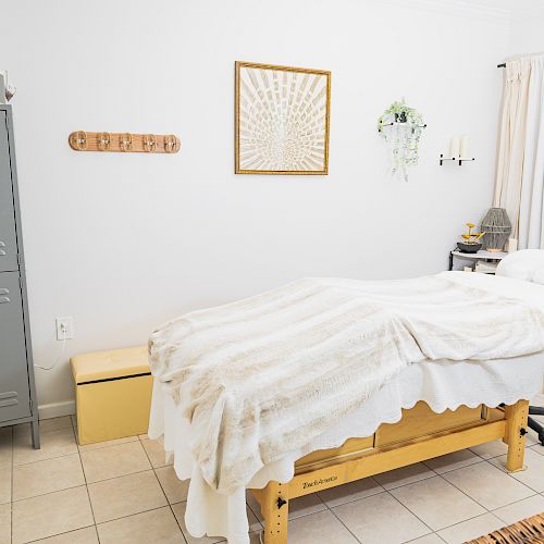 This image shows a cozy massage room with a massage table, locker, small bench, wall decor, and a potted plant, creating a relaxing environment.