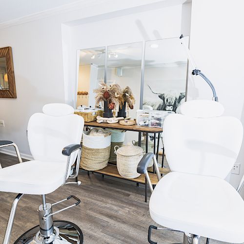 The image shows a bright room with two white salon chairs, a massage bed, a mirror, and various items on shelves.