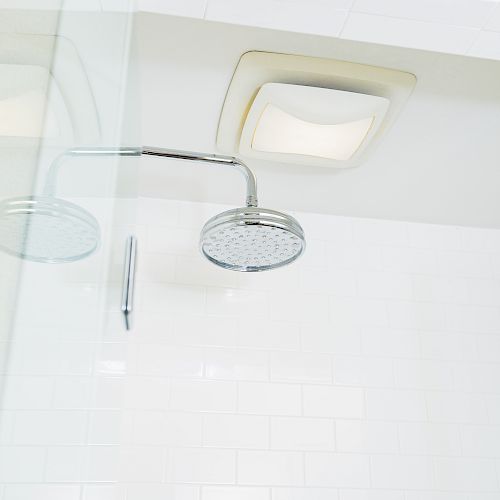 The image shows a modern shower with a circular rain showerhead, white subway tiles, a glass door, and a ceiling light fixture in a bathroom.