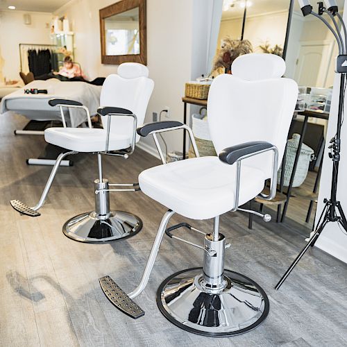 The image shows a clean, modern salon with two white barber chairs, a large mirror, and salon equipment. A person is visible in the background.