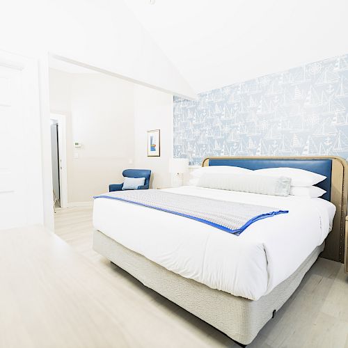 This image shows a bright bedroom with a patterned wall, a neatly made bed, a nightstand, and a lamp, creating a cozy and inviting atmosphere.