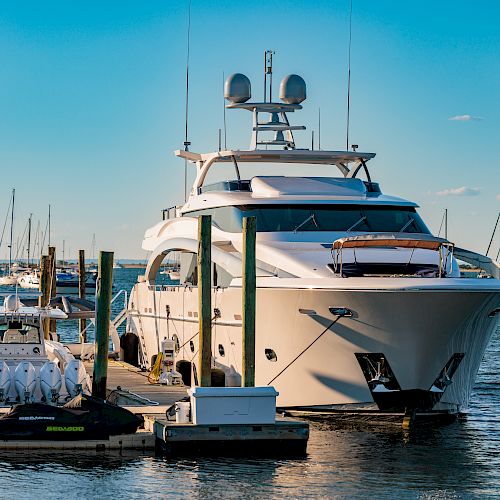 A luxury yacht docked at a marina, with several other boats and sailboats in the background on a sunny day.