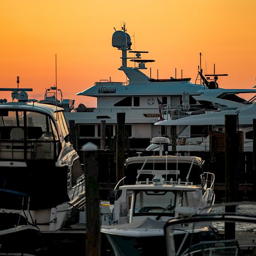 The image shows a marina with several yachts docked against a backdrop of a vibrant orange sunset sky.