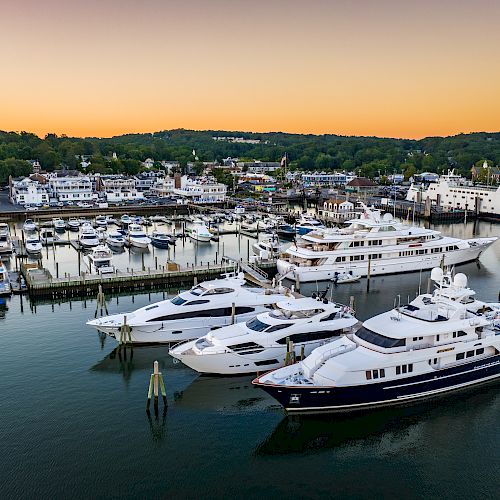 A marina with several yachts docked, surrounded by calm waters and scenic landscape with sunset hues in the background.