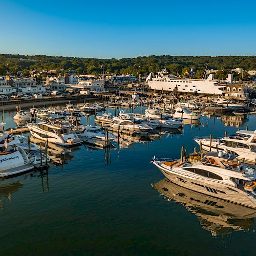 The image shows a marina filled with various yachts and boats docked at piers, with a coastal town and a white ferry in the background.