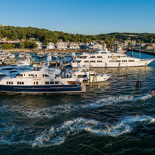 The image shows several large yachts docked at a marina with nearby buildings and greenery. Two people on jet skis are riding in the water.