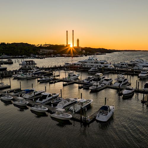 A marina with many boats docked at sunset, with a calm sea, and an orange sky in the background.