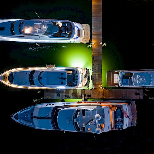 Four yachts are docked at a pier, illuminated by lights, with a green glow in the water beneath them.