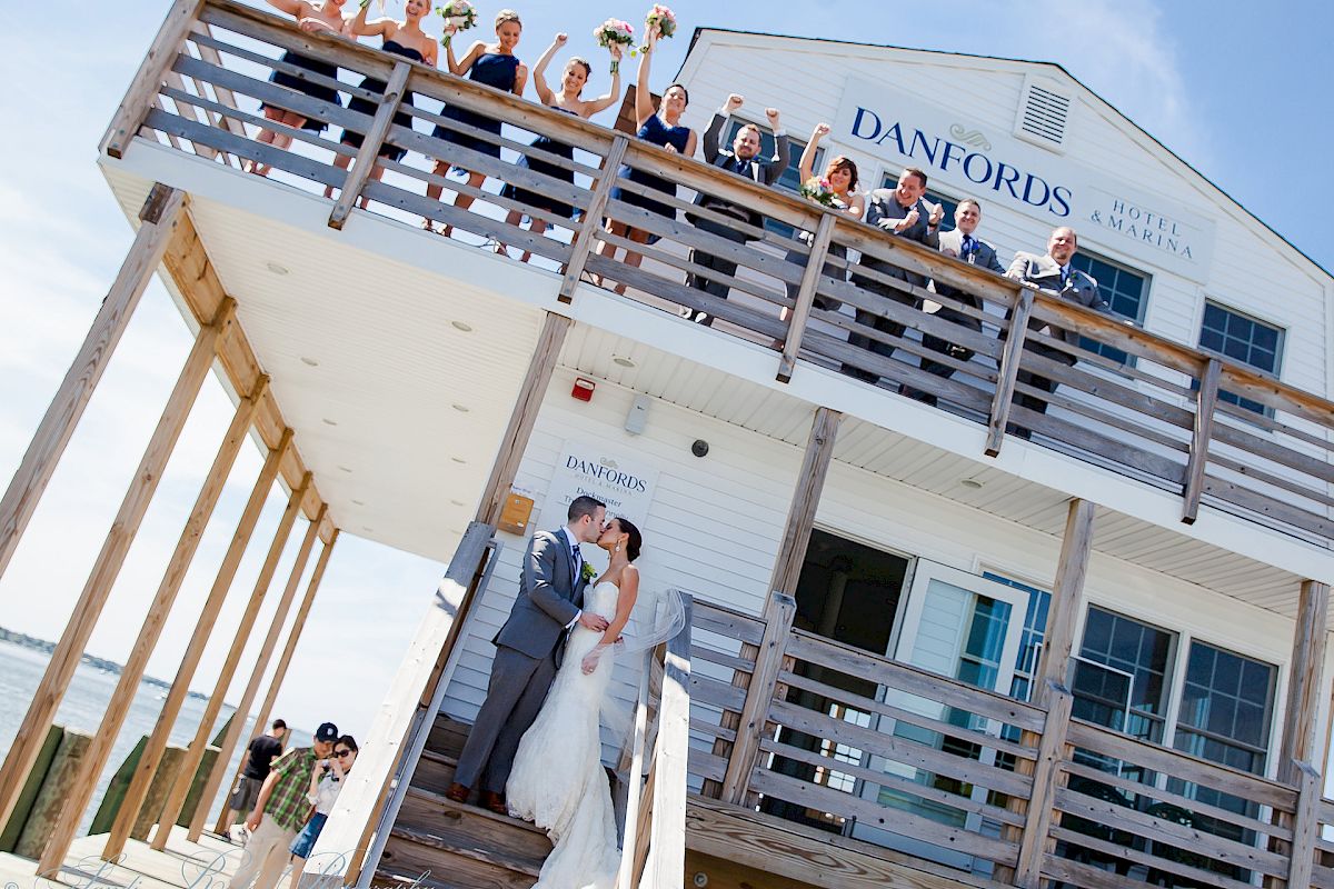 A couple kisses on the stairs of Danfords Hotel & Marina while their wedding party cheers from the balcony above.