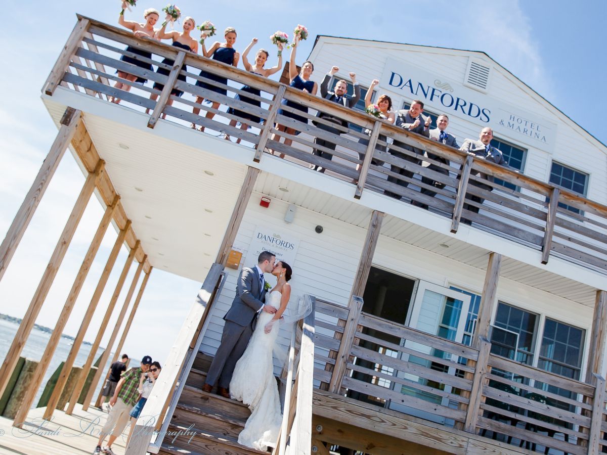 A couple kisses on the stairs of Danfords Hotel & Marina while their wedding party cheers from the balcony above.