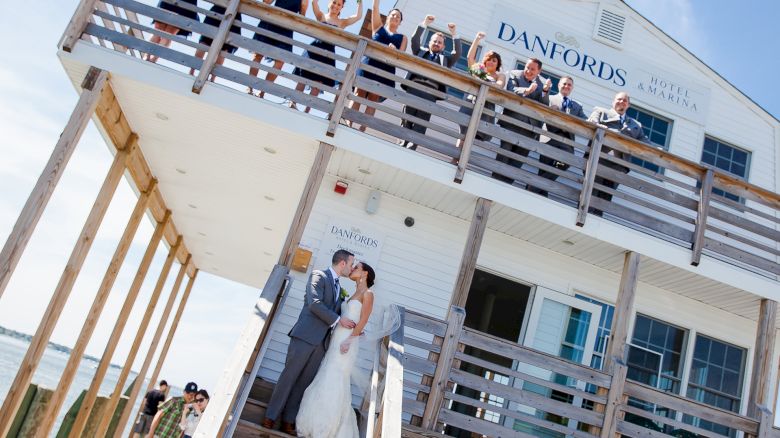 A couple kisses on the stairs of Danfords Hotel & Marina while their wedding party cheers from the balcony above.