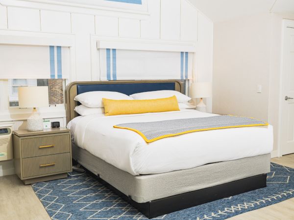 Modern bedroom with neatly made bed, nightstands, and decorative blue rug.