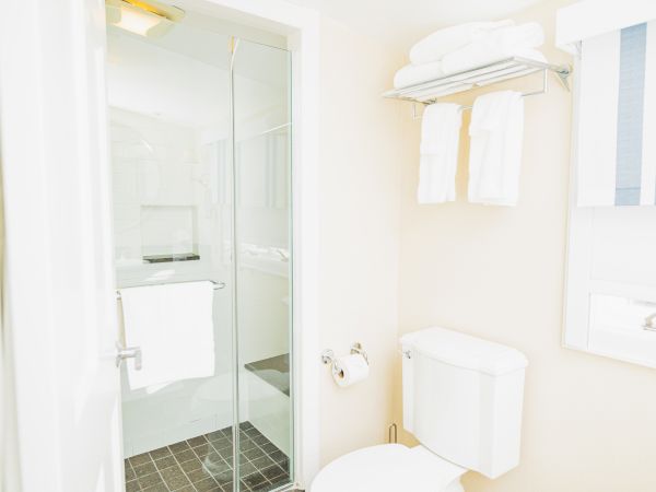 A clean bathroom with a glass-enclosed shower, a toilet, towel rack with towels, and a window with striped blinds is shown in the image.