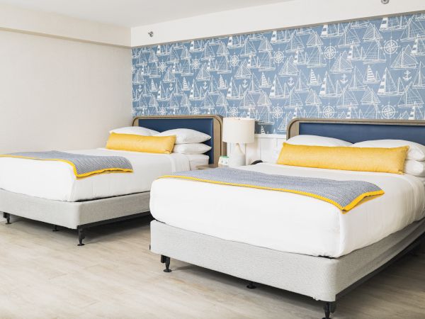 The image shows a modern hotel room with two double beds, blue and white nautical-themed wallpaper, and yellow accents on the bedding, ending the sentence.