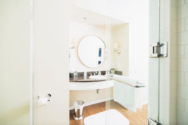 This image shows a modern bathroom with a round mirror, a sink, a towel rack, and wood flooring. The room is bright and minimalistic in design.