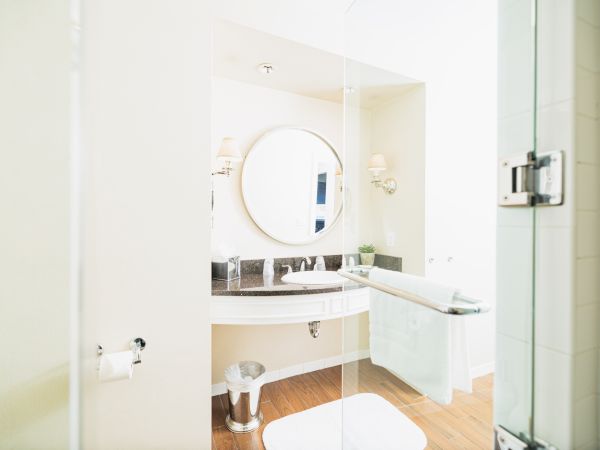 This image shows a modern bathroom with a round mirror, a sink, a towel rack, and wood flooring. The room is bright and minimalistic in design.