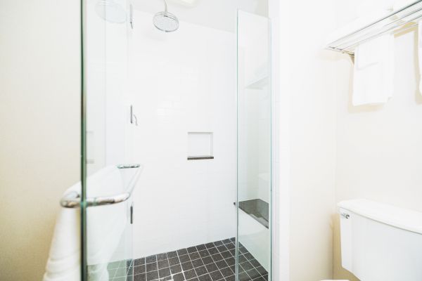 This image shows a modern bathroom with a glass-enclosed shower, white tiles, a toilet, and a towel hanging on a rack above.