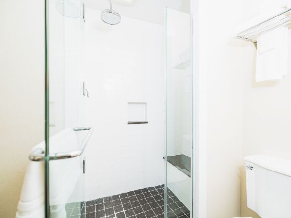 This image shows a modern bathroom with a glass-enclosed shower, white tiles, a toilet, and a towel hanging on a rack above.