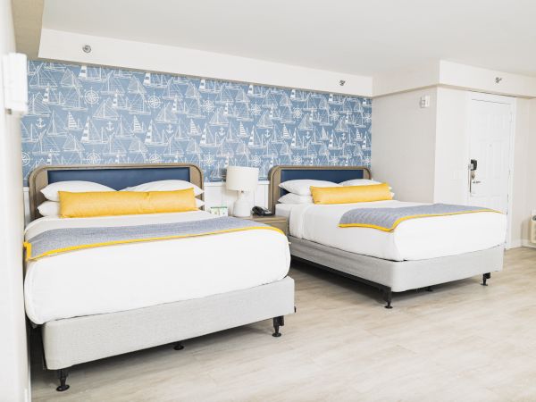 The image shows a hotel room with two double beds, nautical-themed wallpaper, and a soft color scheme, ending the sentence.
