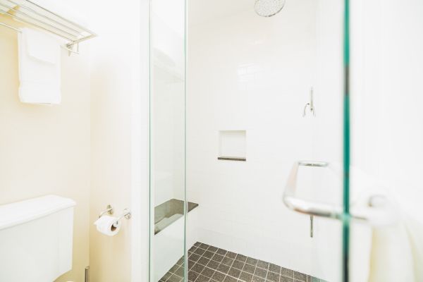 A bathroom with a glass shower enclosure, white tiles, and dark floor tiles; features a towel rack and a toilet with a paper holder.