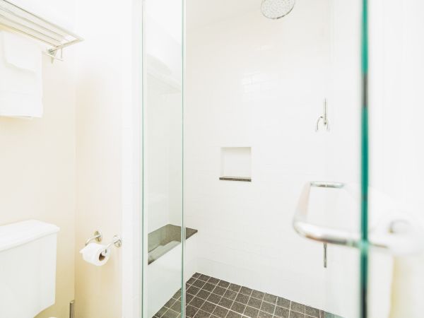 A bathroom with a glass shower enclosure, white tiles, and dark floor tiles; features a towel rack and a toilet with a paper holder.