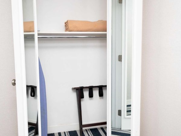 An open closet with folded towels on a shelf, a striped rug, and some shoes/boots near the door.