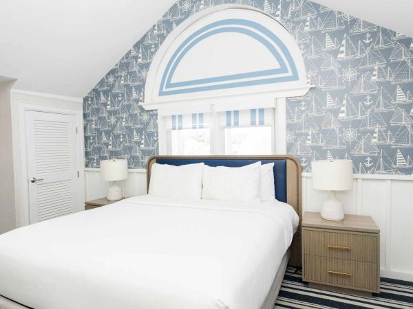 A nautical-themed bedroom with a bed, navy-and-white sailboat wallpaper, a large arch mural, and bedside storage drawers.