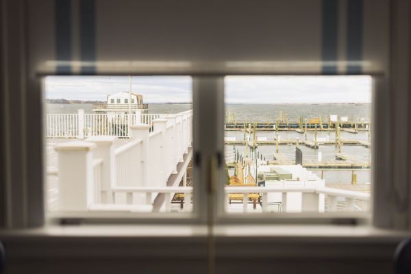 A view of a marina and the ocean through a window with partially open blinds, displaying docks and railings.