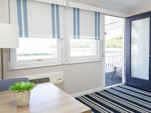 A bright room with large windows, blue-and-white striped blinds, and an open door leading to an outdoor deck.