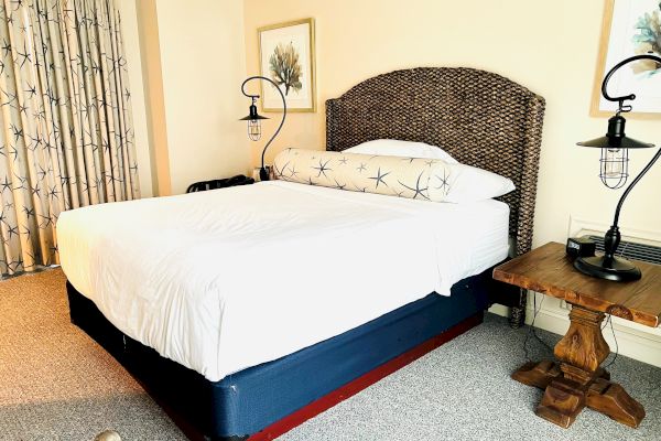 A bedroom featuring a neatly made bed with white linens, two nightstands with lamps, framed artwork, and curtains, all in a cozy setting.