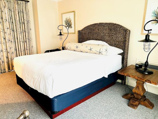 A bedroom featuring a neatly made bed with white linens, two nightstands with lamps, framed artwork, and curtains, all in a cozy setting.