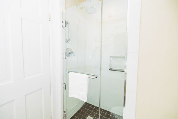 The image shows a modern, enclosed glass shower with a towel hanging on the door handle and a white tiled interior.