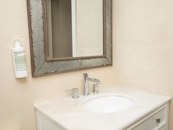 A bathroom vanity with a framed mirror, chrome faucet, soap dispenser, and an illuminated sink.