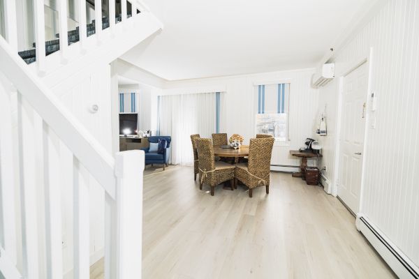 A bright, neatly furnished room with a dining table, four chairs, a blue couch in the background, and white walls with vertical blue-striped windows.